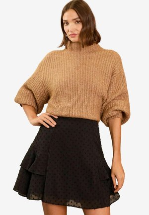 Brauner gestrickter Pullover mit hohem Kragen und kurzen, umgeschlagenen Ärmeln. Schwarzer, geraffter Rock mit strukturierten Punkten und einem gestuften Design.