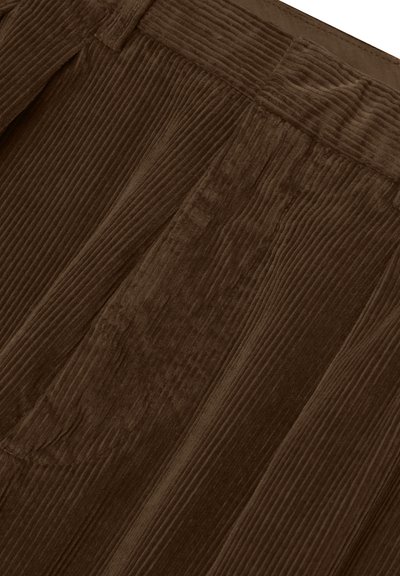 Close-up of brown corduroy fabric with vertical ridges and visible back pocket stitching.