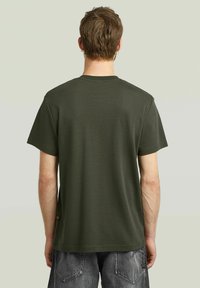 Olijfgroene katoenen T-shirt, korte mouwen, ronde hals, gladde textuur, achterkant gezien, met een klein logo label aan de onderzijde.