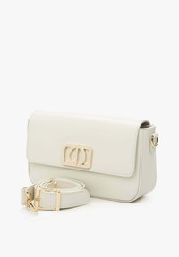 Svetle béžová kožená crossbody taška s magnetickým víkem, zlatými kovovými doplňky a nastavitelným popruhem. Obsahuje logo na přední straně.