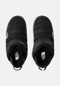 Zapatos negros de slip-on acolchados con textura acolchada, punta redondeada y lengüetas. Presentan el logo de The North Face en blanco en el costado.
