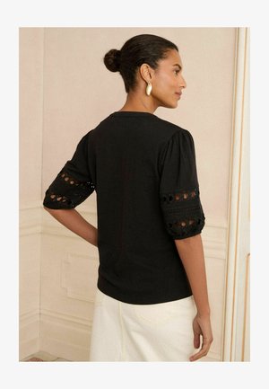 Cămașă neagră cu mâneci bufante, având detalii din dantelă. Designul are o talie strânsă și un decolteu rotund, fiind confecționată dintr-un material moale.