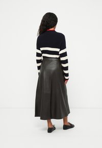 Un pull en tricot à rayures bleu marine et blanches à manches longues, associé à une jupe maxi en cuir noir avec une ceinture et une texture lisse. Chaussures noires avec des accents.