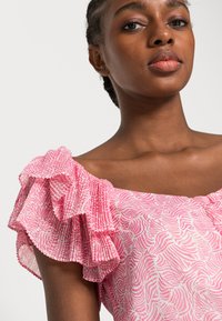 Blusa rosa com padrão, de mangas curtas com babados, apresentando um tecido texturizado e um design ondulado em tons de rosa claro e escuro.