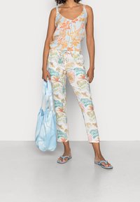 Débardeur bleu clair à motifs floraux avec bretelles fines, pantalon blanc à motifs tropicaux colorés, sac fourre-tout bleu assorti et tongs.