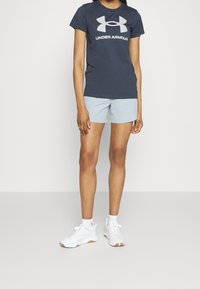 Mörkblå kortärmad Under Armour t-shirt med en stor logotyp, ljusblå shorts och vita sneakers med gummisålar.