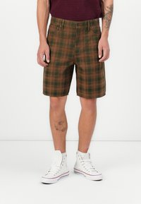 Brune og grøn ternet shorts med lige snit, der har forlommer og knaplukning, parret med hvide høje sneakers.