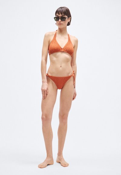 Oranje bikini met textuur, bestaande uit een driehoekige top en broekjes met zijstrikjes. Model draagt een zonnebril. Eenvoudig, sportief ontwerp, geschikt voor badkleding.