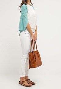 Ljusblå kimono-jacka över vit blus, parat med vita jeans och brun läderväska. Bruna flip-flops med detalj på remmen.