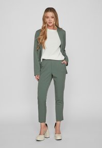 Naistel on kahest osast koosnev kostüüm, mis sisaldab helesinist bleiserit ja sellele sobivaid kitsenevaid pükse. Alfaiselt on seljas kreemjas vardal kootud sviiter. Beezid platvormkingad.