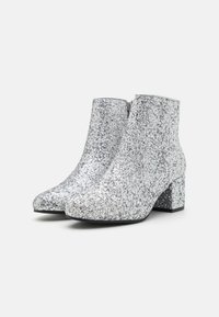 Glittering silver ankle boots with a rounded toe, smooth texture, zip closure, and a chunky heel for stability.