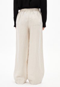 Cremfarbene Leinen-Hose mit weitem Bein, elastischem Bund und einer einzelnen Gesäßtasche, die eine glatte, strukturierte Oberfläche aufweist.