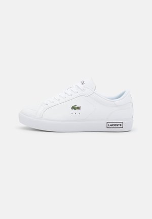 Weiße Lacoste Sneaker mit einem Obermaterial aus strukturiertem Leder, flachen Schnürsenkeln, grünem Krokodil-Logo und einem schwarzen "LACOSTE"-Etikett an der Ferse.
