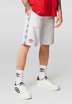 Grå bomuldsshorts med et sort og hvidt diamantmønster langs siden, prydet med et rødt Umbro-logo. Båret med hvide sneakers og sokker.