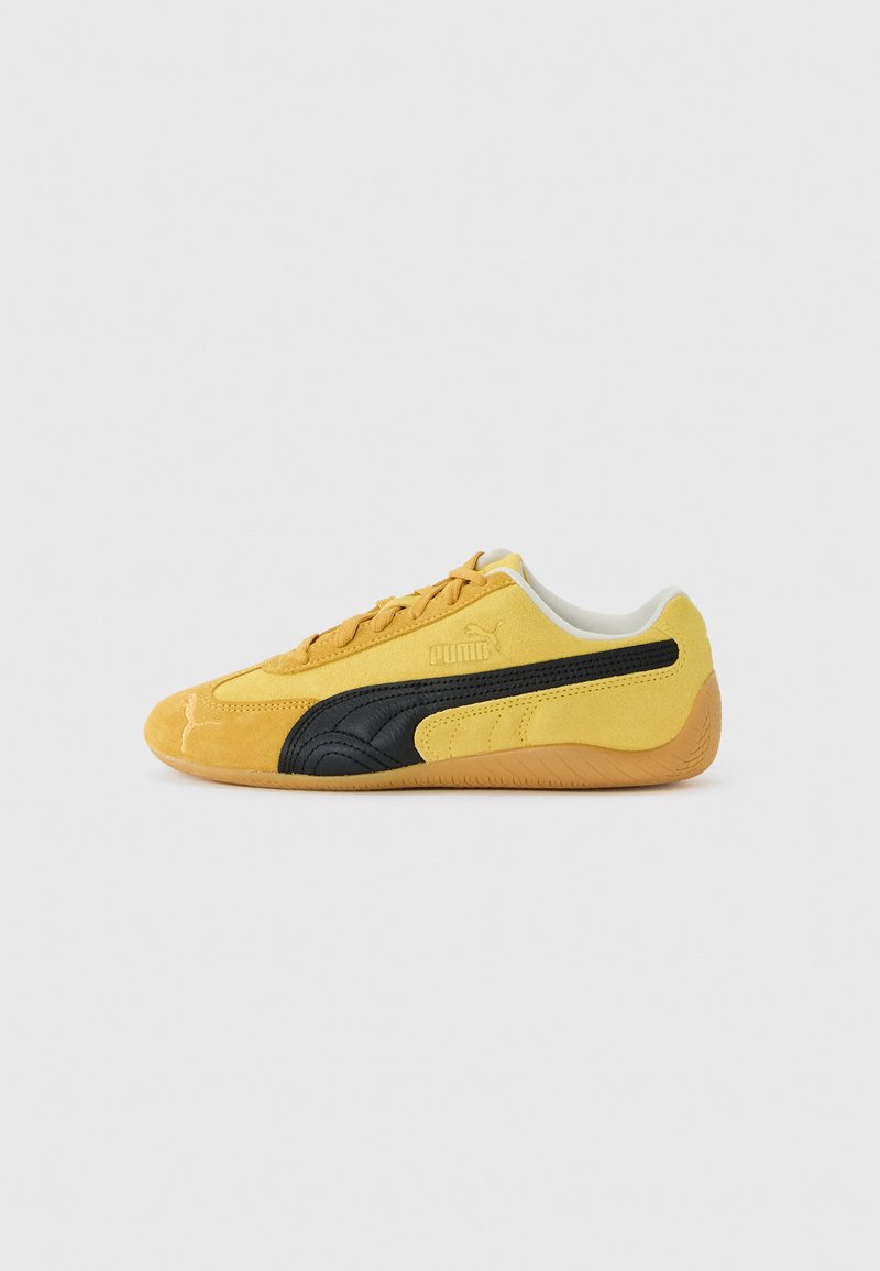 Zapatilla Puma de ante amarillo de perfil bajo con franjas negras a los lados y suela de goma, mostrada en vista lateral sobre fondo blanco.