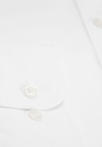 Weißes Hemd mit spitzem Kragen, glatter Textur und zwei runden, weißen Knöpfen mit dezentem Glanz.