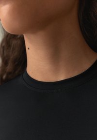 Svart, stretchigt tyg av en topp med hög krage, med slät textur och subtila sömmandetaljer längs halsringningen och axlarna.