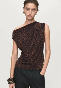 Brown animal print blouse with a draped design and one shoulder. Soft fabric texture, paired with dark denim jeans and chunky bracelets.