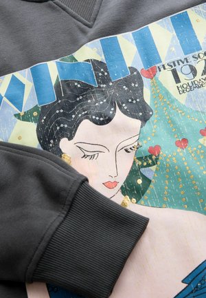 Felpa grigia con un design grafico colorato che raffigura una donna con capelli neri, adornata di paillettes e con un motivo di albero di Natale.