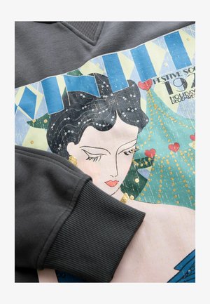 Felpa grigia con un design grafico colorato che raffigura una donna con capelli neri, adornata di paillettes e con un motivo di albero di Natale.