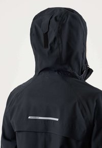 Čierna nepremokavá bunda s kapucňou, zadné zapínanie na suchý zips a reflexná páska s nápisom "Swedemount" na hornom chrbte.