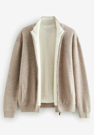 Beige tõmblukuga jakk, millel on pehme kreemjas fliisvooder, küljetaskud, soonikkoes mansetid ja mugav lõige. Valmistatud tekstuurilisest kudumikiust.