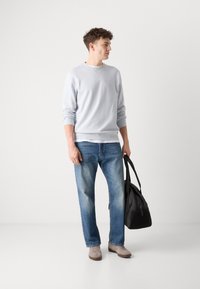 Sudadera azul claro, corte relajado, cuello redondo, combinada con jeans azul claro. Zapatillas gris claro, llevando una bolsa de deporte negra.