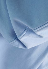 Tela azul claro que muestra una textura suave con un ligero brillo. El material es suave, con detalles visibles de costuras y pliegues suaves.