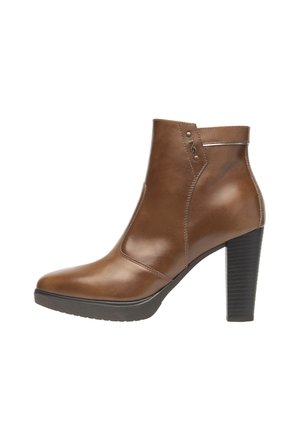Bottines en cuir marron avec un bout pointu, un talon bloc haut et des accents cousus. Comprend des petits détails métalliques près de la cheville.