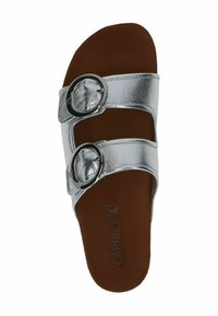 Silvriga lädersandaler med två breda remmar, var och en med en rund metallspänne, som vilar på en brun fotbädd.