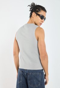 Grå ribbet ärmløs topp med et tettsittende design, kombinert med løse blå denimjeans. Stoffet ser glatt ut, mens snittet fremhever skuldrene.