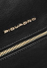 Borsa in pelle nera texturizzata con zip dorata e dettaglio del logo. La cerniera ha denti distinti, che conferiscono un tocco funzionale.