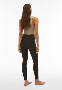 Leggings neri realizzati in materiale elastico, a vita alta con una texture liscia e un dettaglio tasca sul retro. Abbinati a una maglietta sportiva beige.