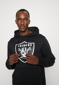 Sudadera negra con un gran gráfico de los Raiders en blanco en el pecho. Cuenta con capucha con cordón y bolsillo frontal. Textura de tela suave.