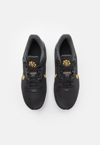 Une paire de chaussures de sport noires avec des broderies dorées et des lacets, vue de dessus sur un fond blanc.