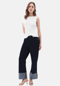 Vit ribbad ärmlös topp, mörk denimjeans med grå uppvikning och gul accent, samt beige remsandaler med klack.
