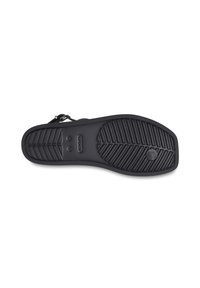 Semelle de sandale noire en caoutchouc texturé, avec un motif rainuré et une caractéristique circulaire centrale. Logo de la marque "crocs" visible à la surface.