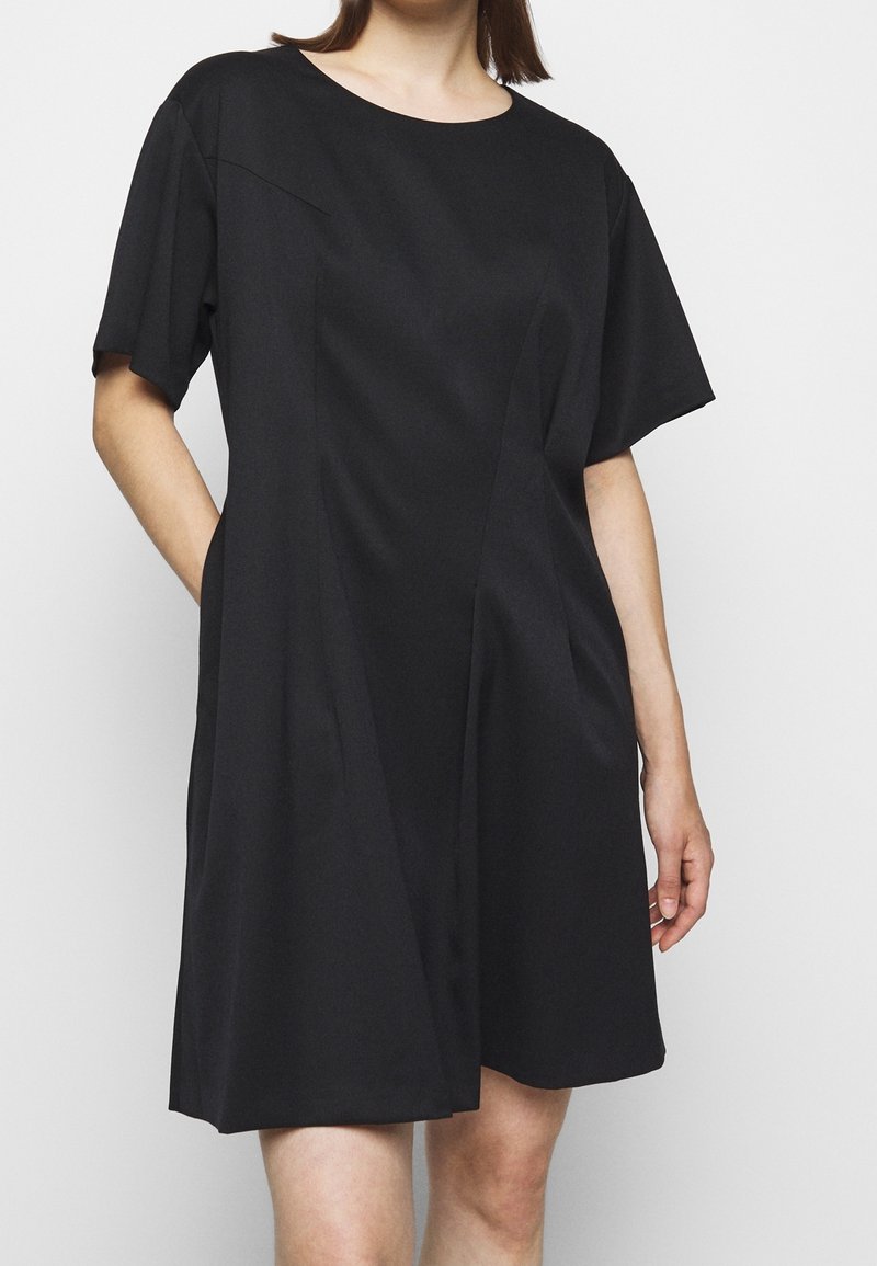 Vestido negro de manga corta con cuello redondo. Textura suave, a la altura de la rodilla con un corte estructurado y bolsillos laterales. Diseño minimalista.