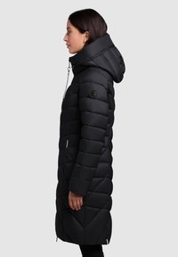 Black puffer coat with a quilted design, long silhouette, and an adjustable hood. Features a logo patch on the sleeve and zippered pockets.