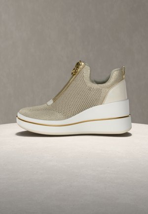 Chaussure beige à enfiler avec dessus en maille, accent zippé doré et semelle compensée blanche bordée d'une finition dorée. Détails texturés sur le dessus.