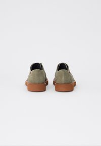 Pantofi din suede verde, cu vârf rotunjit și talpă din cauciuc marron, având un design minimalist și un accent cusut aproape de toc.