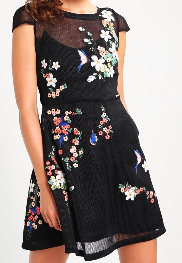 Svart blommigt broderad klänning med åtsittande liv, korta ärmar och utsvängd kjol. Har färgglada blommönster och mesh-textur.