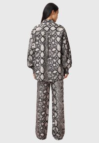 Ensemble deux pièces comprenant un chemisier à manches longues avec imprimé serpent et un pantalon à jambes larges dans des nuances de gris et de noir, avec un motif texturé.