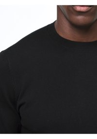 Svart kortärmad T-shirt, tillverkad av en mjuk bomullsblandning, med rund hals och en figurnära silhuett. Diskret sömnadsdetalj på axlarna.