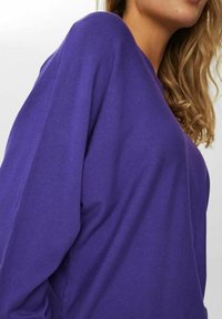 Lila langärmeliges Oberteil mit lockerem Schnitt, glatter Textur und überschnittenen Schultern. Minimalistisches Design ohne sichtbare Beschläge.