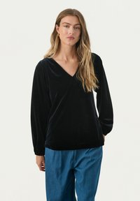 Zwart fluwelen langemouwtop met een V-hals, zachte textuur en een relaxte pasvorm, gecombineerd met losse blauwe spijkerbroek.