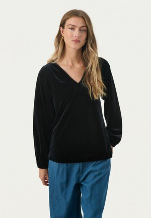 Schwarzes Samtoberteil mit langen Ärmeln und V-Ausschnitt, weicher Textur und lässigem Schnitt, kombiniert mit lockeren blauen Jeanshosen.