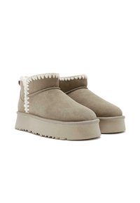 Botas de tobillo de ante marrón con un ribete texturizado blanco, punta redondeada y suela gruesa con una banda de rodadura estampada.
