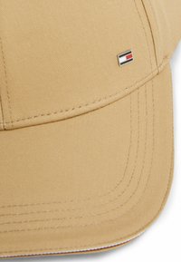 Cappellino da baseball beige con visiera strutturata, dettagli cuciti e un piccolo logo rettangolare sul davanti nei colori rosso, bianco e blu.