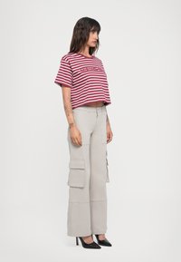 Gestreepte crop top in bordeauxrood en wit, gecombineerd met beige cargobroek met zakken, en zwarte hoge hakken.
